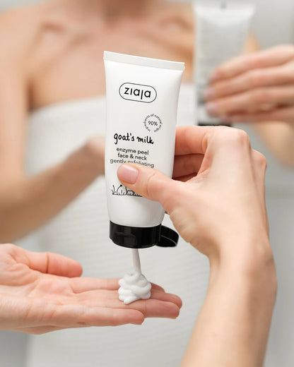 A hand holds a white tube of Ziaja Goal's Milk enzyme peel face & neck cream, squeezing a dollop of white cream into another hand, with a blurred bathroom mirror reflection in the background.