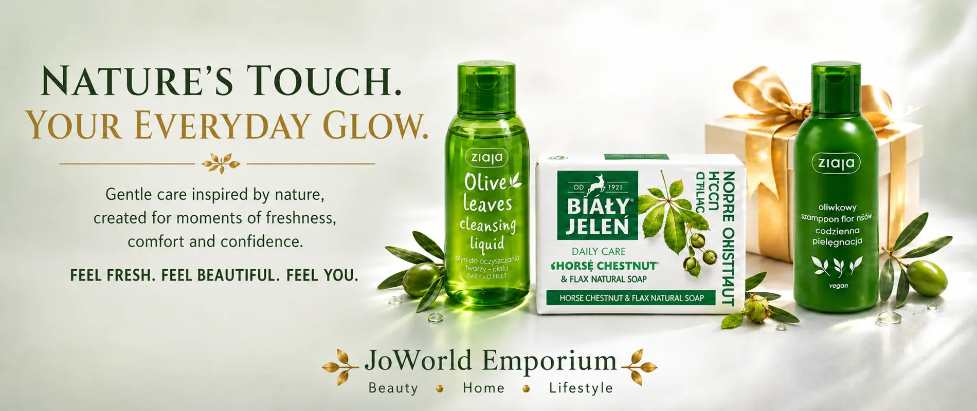 Three JoWorld Emporium skincare products displayed together on a light beige background: a green bottle of olive leaf cleansing liquid, a green and white box of Bialy Jelen daily care soap, and a green bottle of coconut oil body wash next to a gold gift box. Text on the left reads 'Nature's Touch.