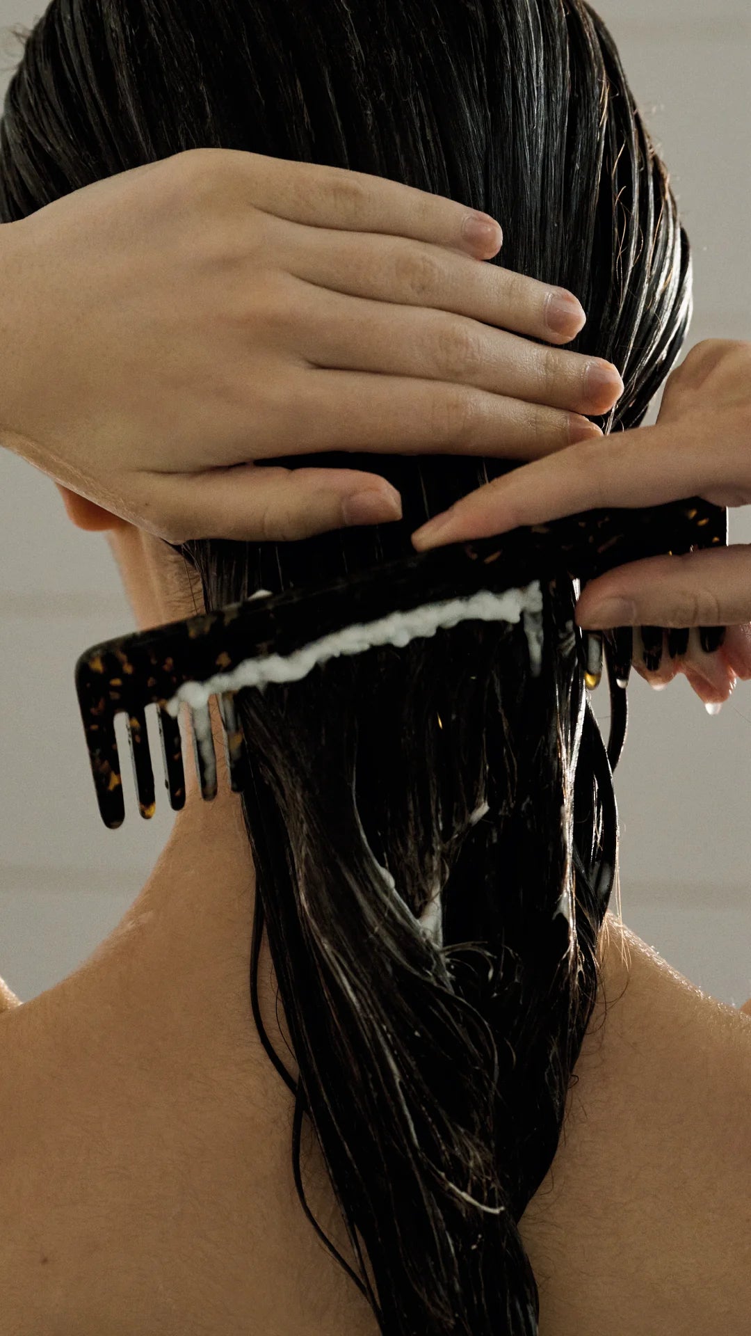 Person combing wet hair with a black comb against a neutral background